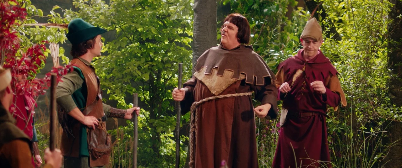 Stan & Ollie (2018) movie still: fullbody — Three men dressed in medieval costumes stand among green trees and dense foliage. The men converse while…