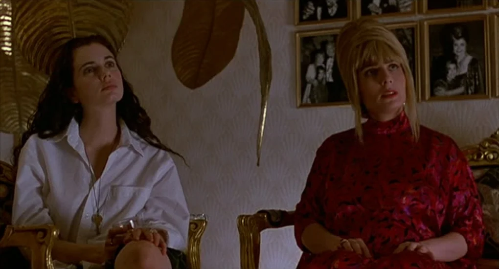 Exotica (1994) movie still: medium — An interior living space features patterned wallpaper, gold-toned chairs, and framed black-and-white family…