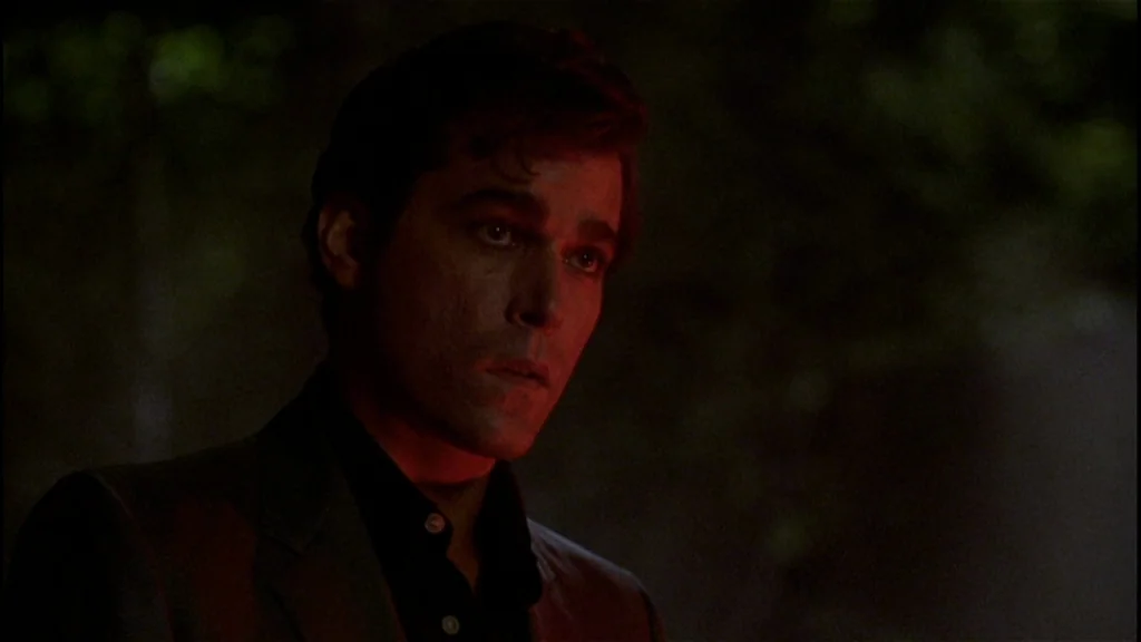 Goodfellas (1990) movie still: closeup — A dark, blurred outdoor space at night with indistinguishable background shapes. A man stares ahead, his…