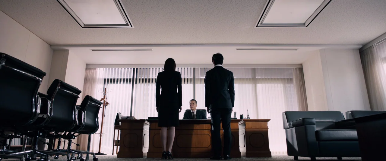 Shin Ultraman (2022) movie still: wide — A wide, low-angle shot of a minimalist high-rise suite with floor-to-ceiling windows. Two people stand…