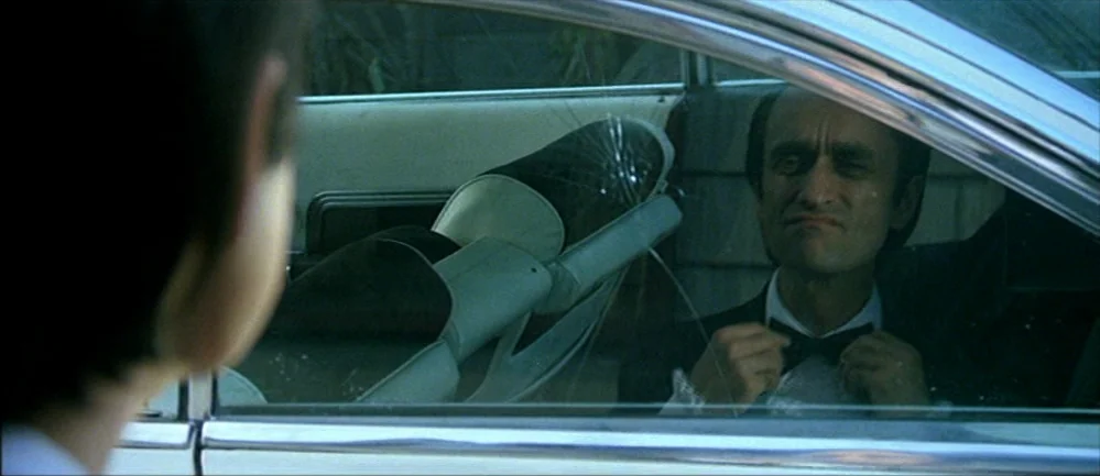 The Deer Hunter (1978) movie still: medium — A man sits inside a vehicle with a cracked windshield looking out toward someone. The man is wearing…
