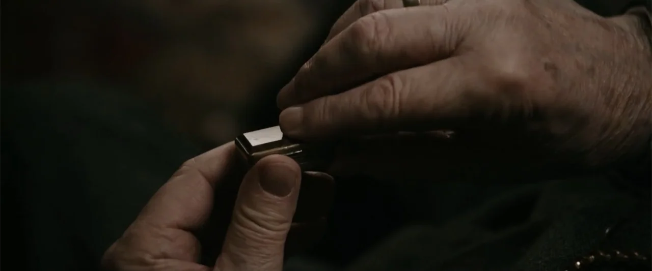 Freud's Last Session (2023) movie still: closeup — An interior space provides a dark background for a pair of hands. The hands manipulate a small…