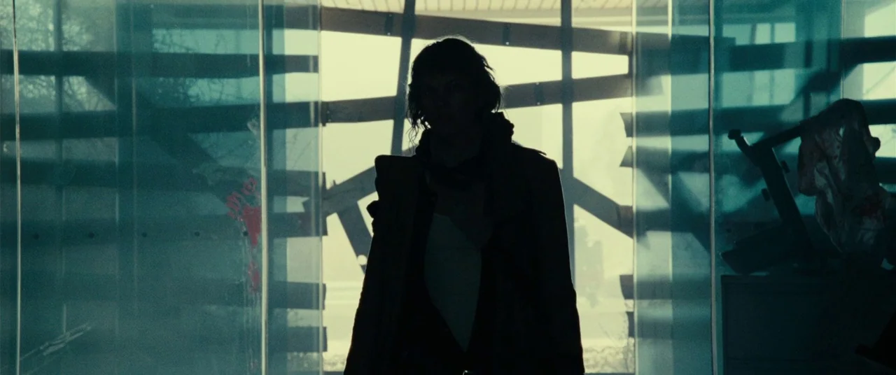 Resident Evil: Extinction (2007) movie still: medium — A woman stands centered before a large floor-to-ceiling glass wall with metal structural…