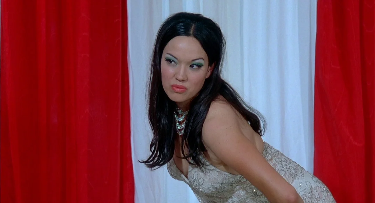 Viva (2007) movie still: medium — A woman stands in front of alternating vertical red and white fabric curtains. The subject leans slightly forward…