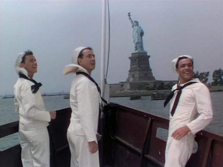 On The Town (1949) movie still: fullbody — Three sailors stand on the deck of a boat moving through harbor waters. The Statue of Liberty is clearly…