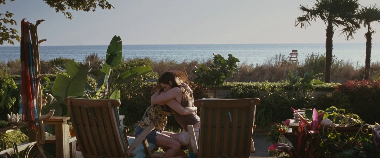 The Twilight Saga: Eclipse (2010) movie still: wide — A seaside patio overlooks the ocean with palm trees and dense vegetation surrounding them. Two…