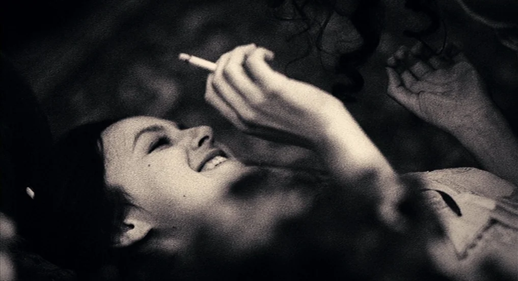 House of Tolerance (2011) movie still: closeup — A dark, dimly lit environment features a woman lying on a soft surface. She reclines with her head…