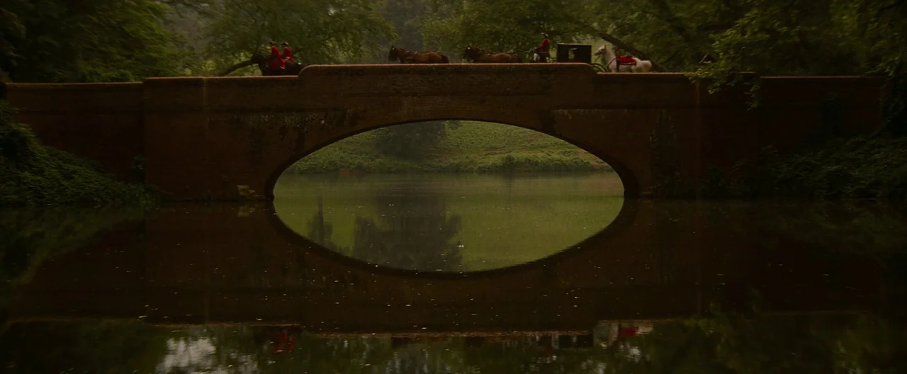 The Last of the Mohicans (1992) movie still: wide — An arched brick bridge spans a still, reflective lake surrounded by dense green trees. A…