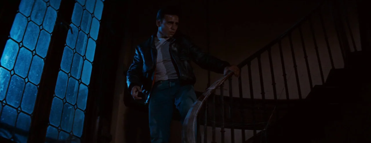 Rebel Without A Cause (1955) movie still: medium — A dark, dimly lit indoor stairwell features a curved wooden bannister and ornate leaded windows.…