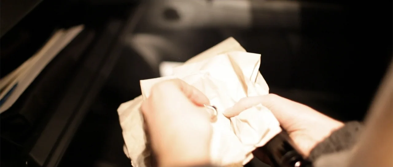 La coherencia del caos movie still: closeup — The interior of a dark vehicle is visible with a black glove compartment door visible. A pair of hands…