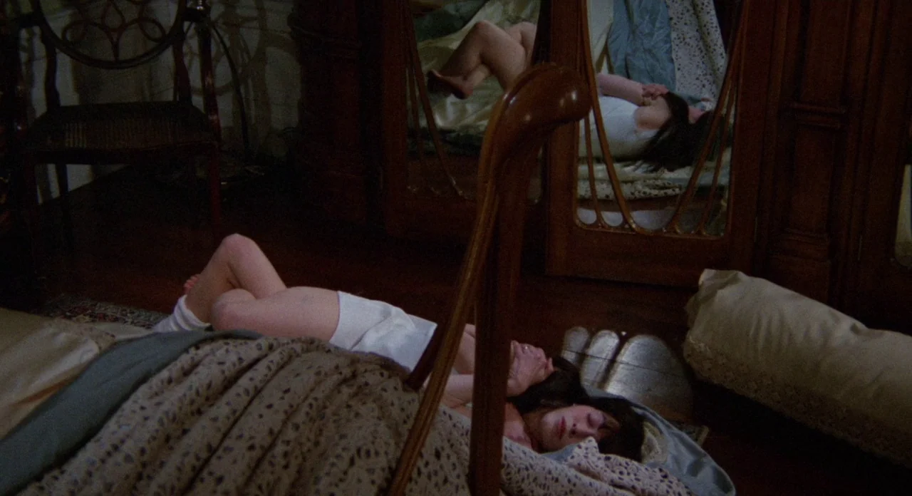 Secret Ceremony (1968) movie still: medium — A dimly lit room contains a large wooden wardrobe with mirror panels. A young woman lies on the floor…