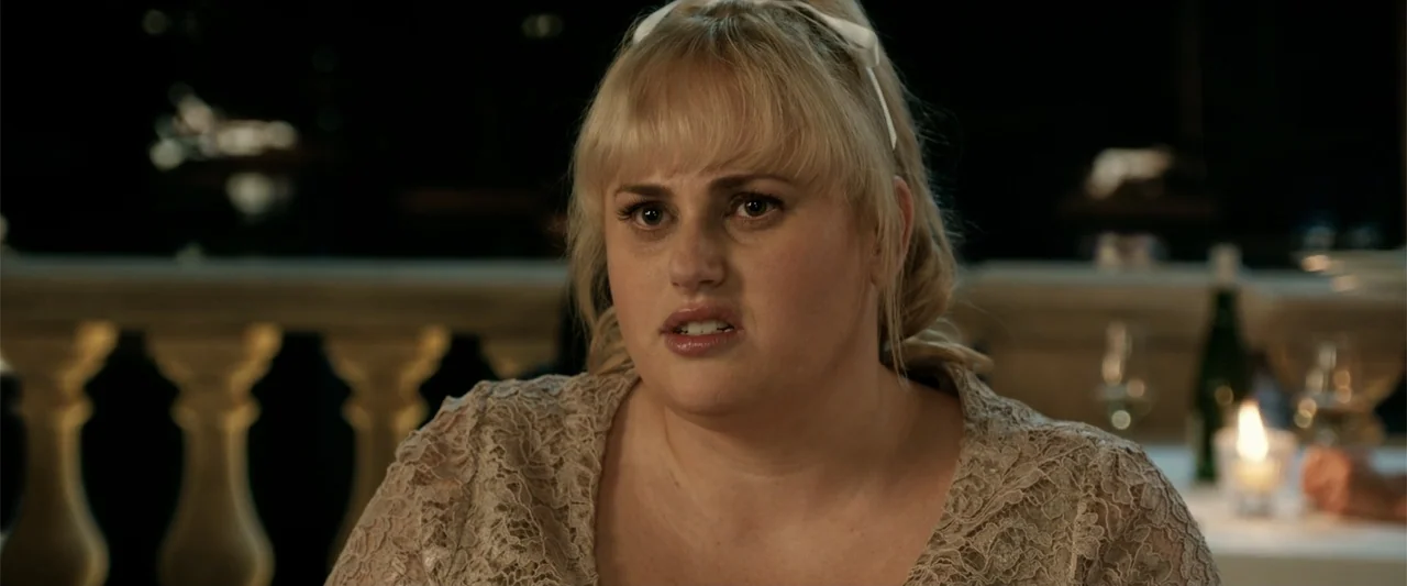 The Hustle (2019) movie still: closeup — A night terrace setting with a stone balustrade visible in the soft-focused background. A blonde woman in a…