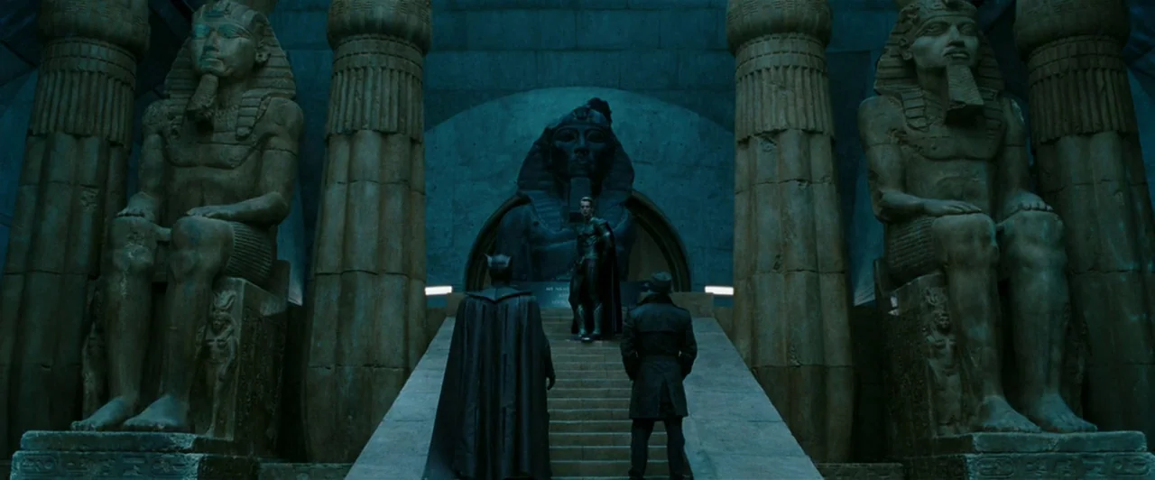 Watchmen (2009) movie still: wide — A dark, expansive hall features massive Egyptian stone pharaoh statues flanking a central staircase. Three men…