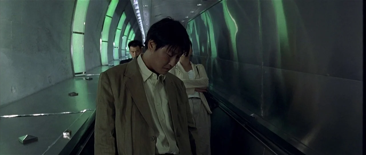 Sympathy for Mr. Vengeance (2002) movie still: medium — An escalator moves through a curved tunnel lined with glowing green translucent panels. A…