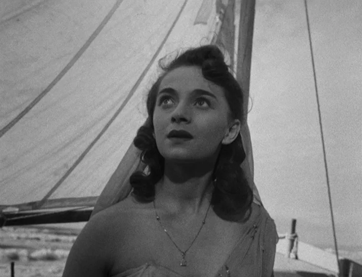 The White Sheik (1952) movie still: medium — A woman stands on the deck of a sailboat under a white sail. She looks toward the sky with her head…