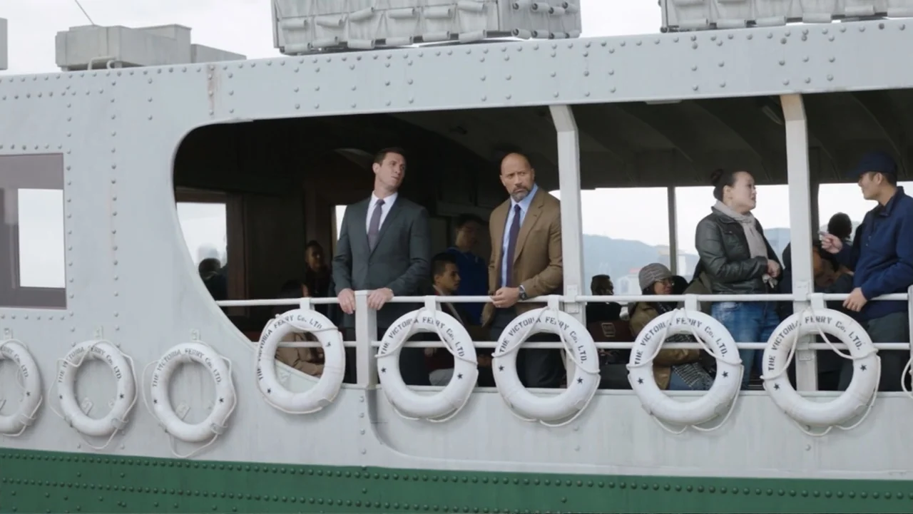 Skyscraper (2018) movie still: medium — The deck of a ferry with rows of white lifebuoys lining the metal railings. Several passengers in business…