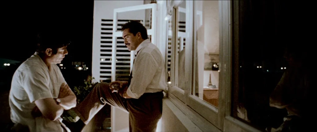 Che Part 1 (The Argentine) (2008) movie still: medium — A night balcony overlooks a dark exterior with light spilling from a window. Two men in…