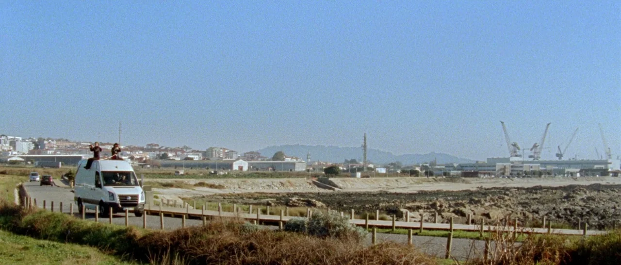 Arabian Nights: Volume 1 – The Restless One (2015) movie still: wide — A white van moves along a coastal road near an industrial shoreline with…
