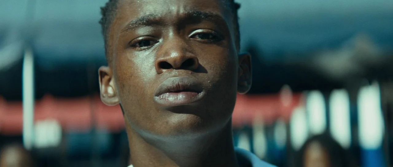 Moonlight (2016) movie still: closeup — An outdoor area features structures with red and blue painted sections in the background. A teenage boy with…