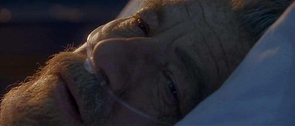 Apt Pupil (1998) movie still: closeup — An elderly man rests his head on white pillows in a dimly lit space. A clear nasal cannula tube runs across…