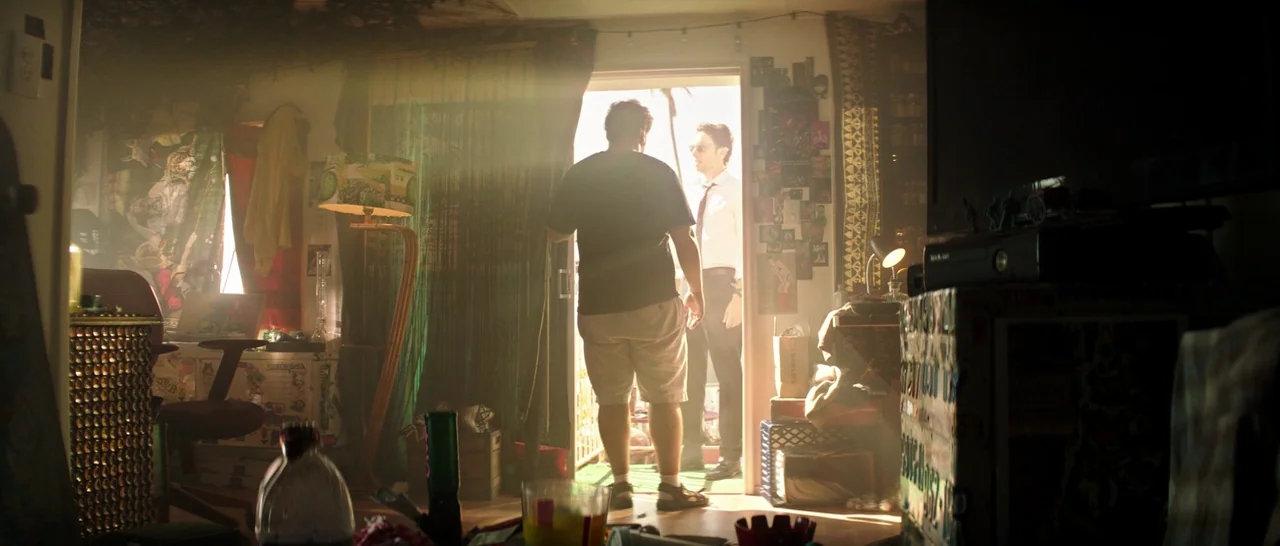 Wish I Was Here (2014) movie still: medium — A cluttered apartment interior is bathed in bright daylight coming through an open doorway. A man in a…
