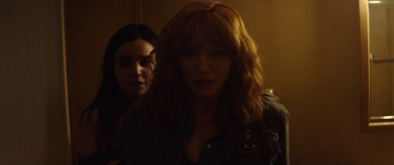 The Strangers: Prey at Night (2018) movie still: medium — A dimly lit room with brown walls and a small rectangular wall mirror. Two women stand in…