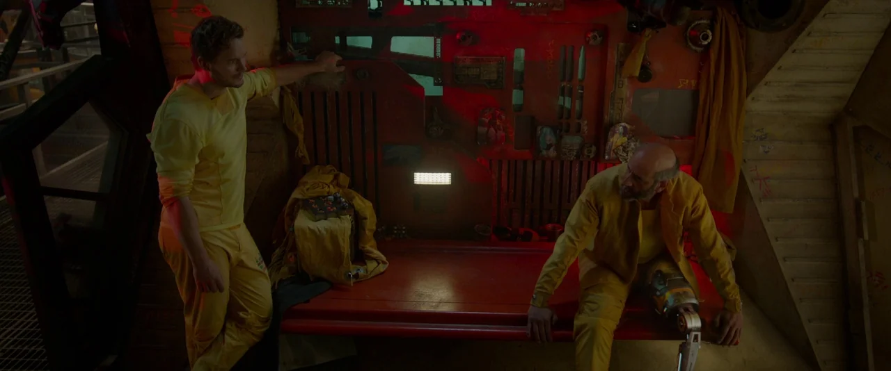 Guardians of the Galaxy (2014) movie still: wide — A dimly lit industrial prison cell features red metal walls and a built-in bench. Two men wearing…