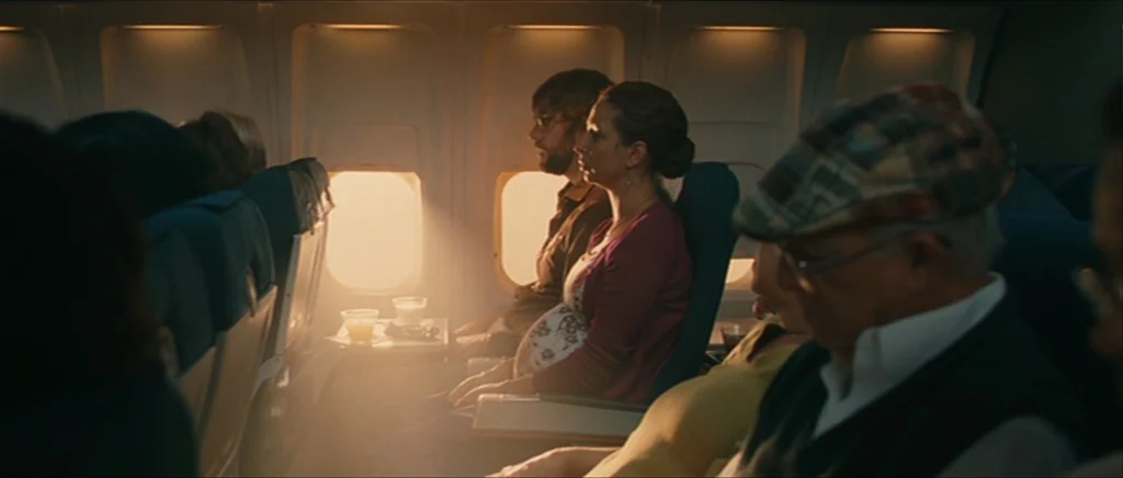 Away We Go (2009) movie still: medium — The interior of an airplane cabin is filled with warm, glowing sunlight through windows. A pregnant woman…