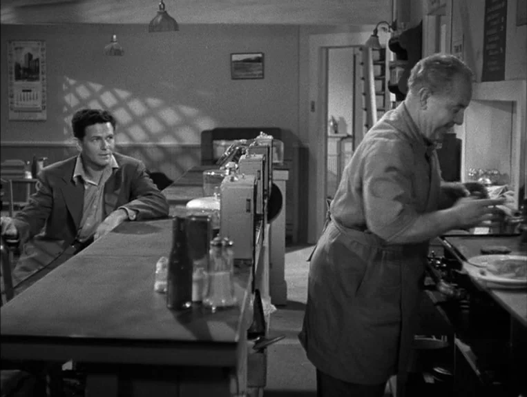 The Postman Always Rings Twice (1946) movie still: medium — A small diner interior features a counter, stools, and wall-mounted menus. A man sits at…