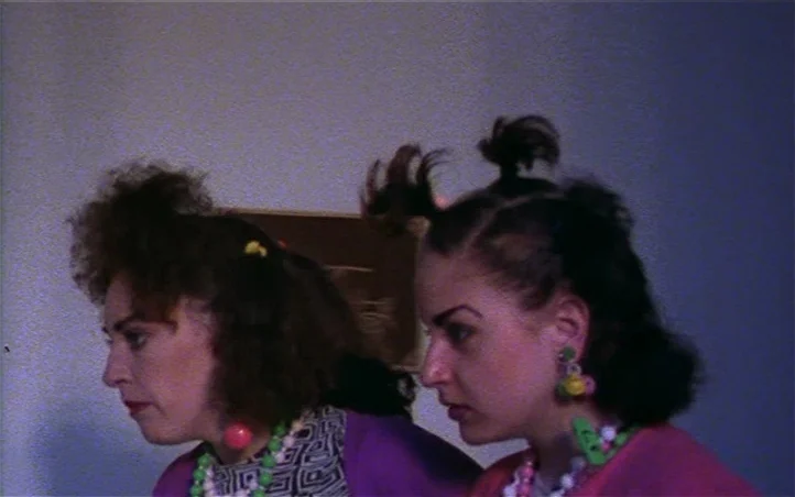 Pepi, Luci, Bom and Other Girls Like Mom (1980) movie still: medium — Two women with stylized hair and colorful jewelry stand indoors against a…