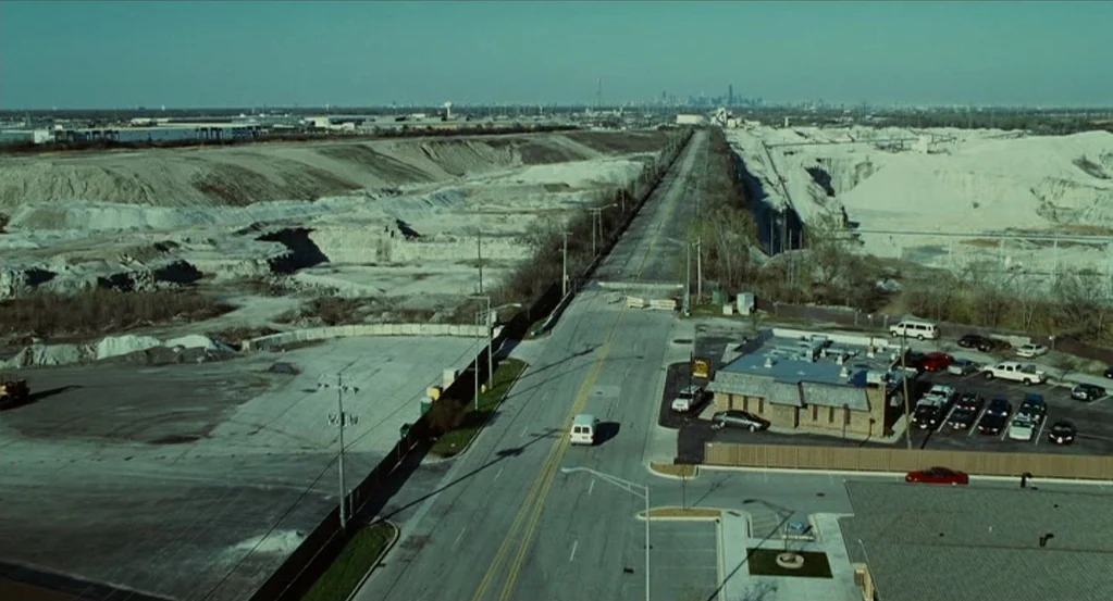 Source Code (2011) movie still: establishing — An aerial view of an industrial road surrounded by extensive piles of white aggregate material. A…