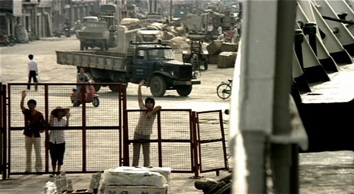 The Boys From Fengkuei (1983) movie still: wide — A bustling industrial dock area sits adjacent to the edge of a large ship. People stand behind a…