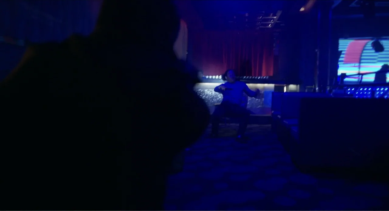 Instantes Capturados (2022) movie still: medium — A dimly lit nightclub features a central bar area bathed in deep blue light. A man sitting in the…