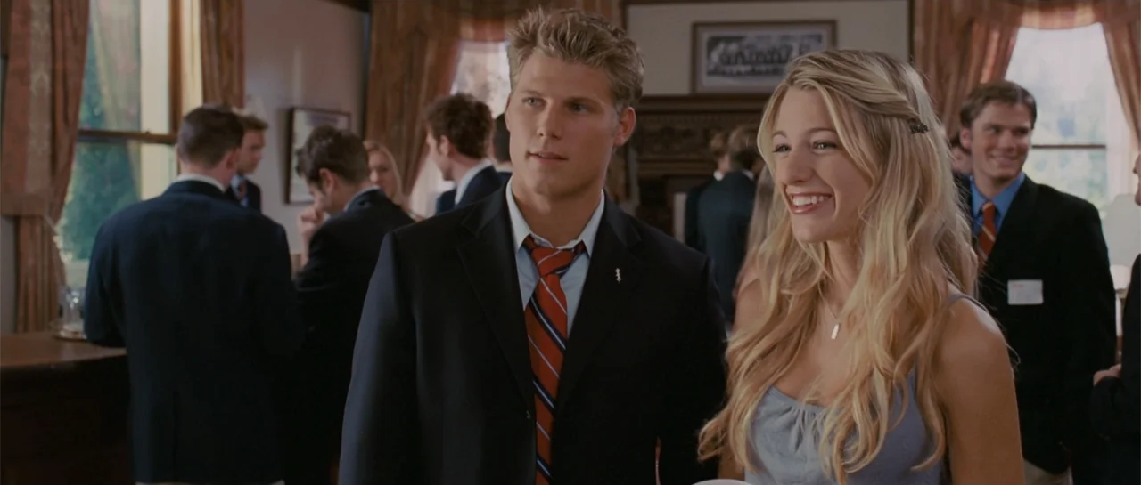 Accepted (2006) movie still: medium — A well-lit indoor gathering room contains numerous people wearing formal suits and dresses. A young man and a…