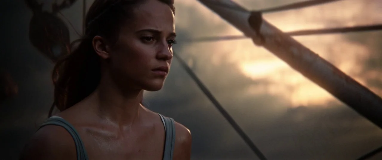 Tomb Raider (2018) movie still: medium — A woman stands on a boat deck during golden hour with a structural metal frame behind her. She looks toward…
