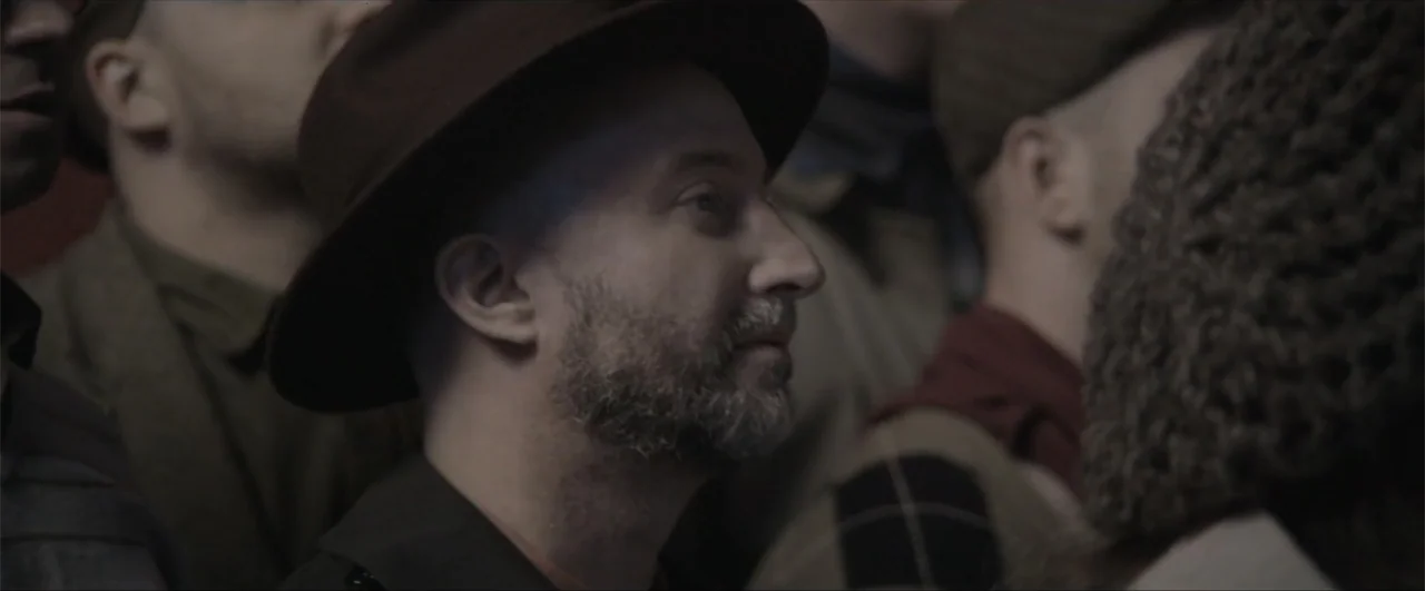 Behind the Line: Escape to Dunkirk (2020) movie still: closeup — A dense group of people stands closely together in an indoor setting. A man wearing…