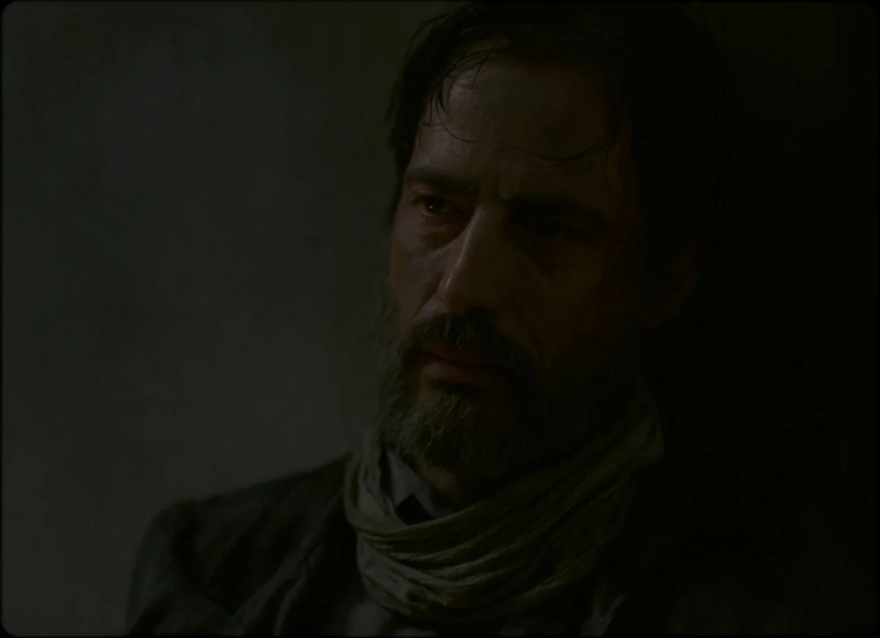 Son of Saul (2015) movie still: closeup — A dark, spartan interior environment features a single man pressed against a rough wall. The man stares…