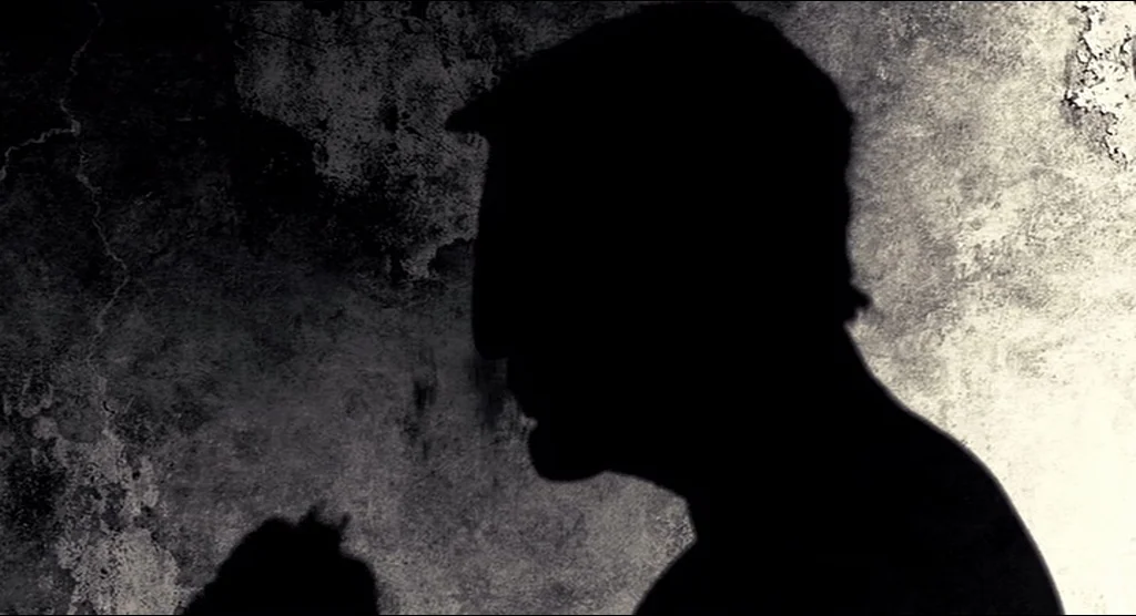 Sin City (2005) movie still: closeup — A dark, textured concrete or plaster wall serves as the backdrop. A silhouette of a human head and shoulders…