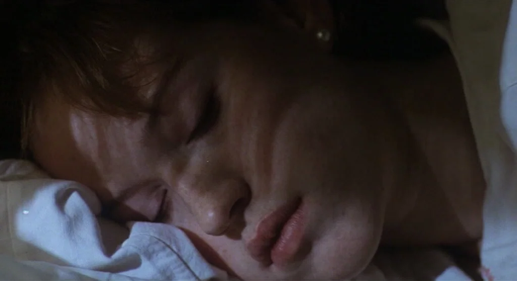 King Lear (1987) movie still: closeup — A close view of a person sleeping in a dark bedroom environment. The individual is resting their head on a…