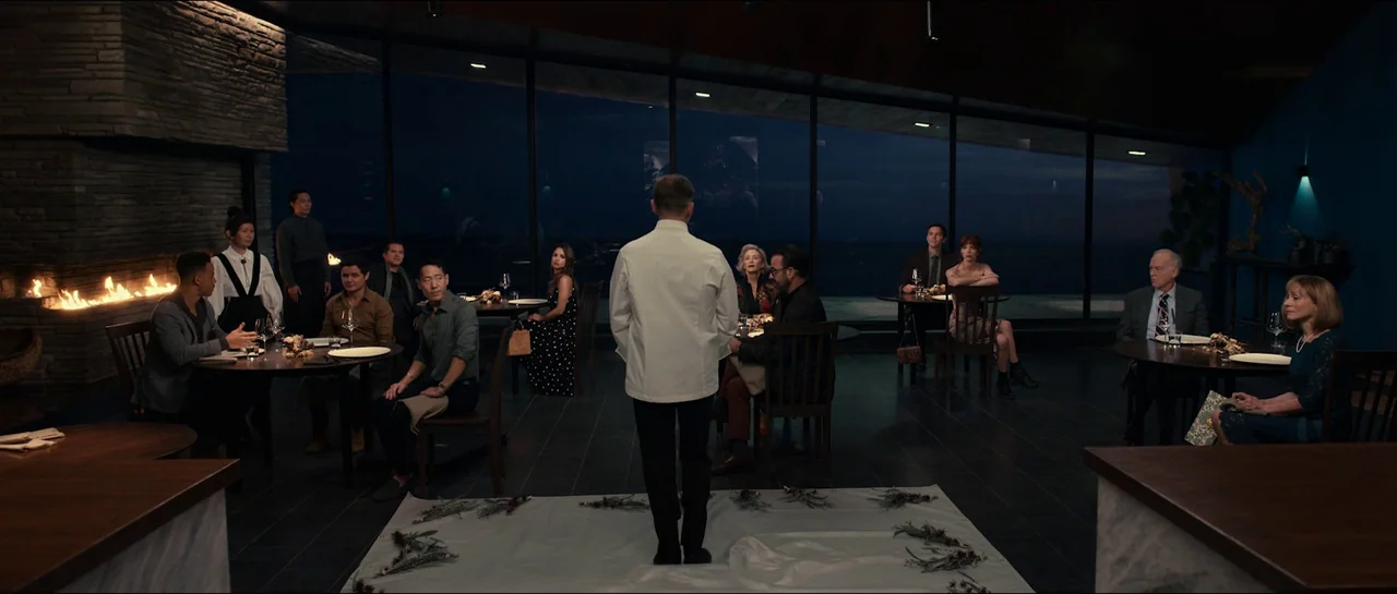 The Menu (2022) movie still: wide — A minimalist modern restaurant features floor-to-ceiling glass walls overlooking a dark ocean at night. A lone…