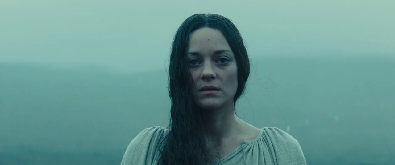Macbeth (2015) movie still: closeup — A woman stands in front of a distant, fog-covered landscape during a cloudy day. She faces the camera directly…
