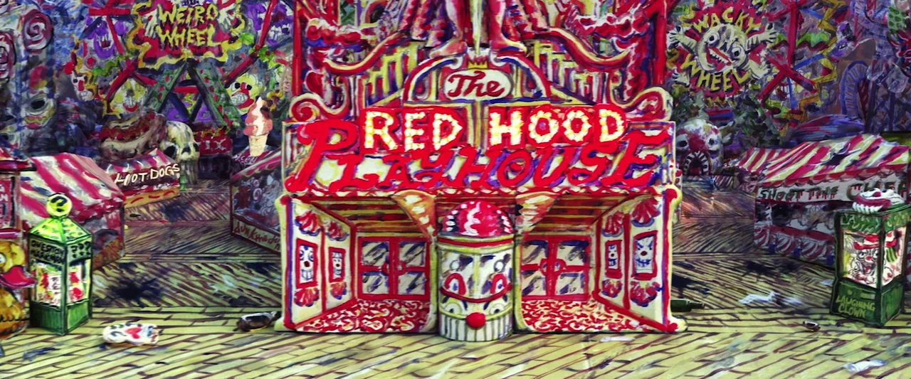 The People’s Joker (2022) movie still: wide — A miniature handmade carnival set features a central structure labeled The Red Hood Playhouse. Painted…