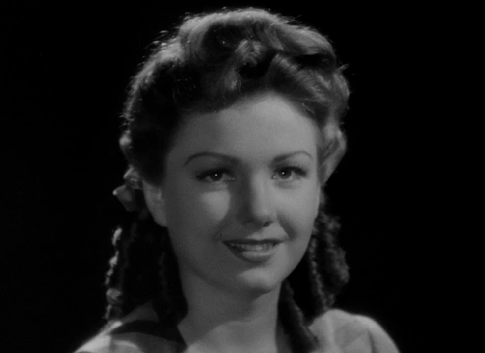 The Magnificent Ambersons (1942) movie still: closeup — A woman's face is centered against a solid black backdrop. She smiles slightly while looking…