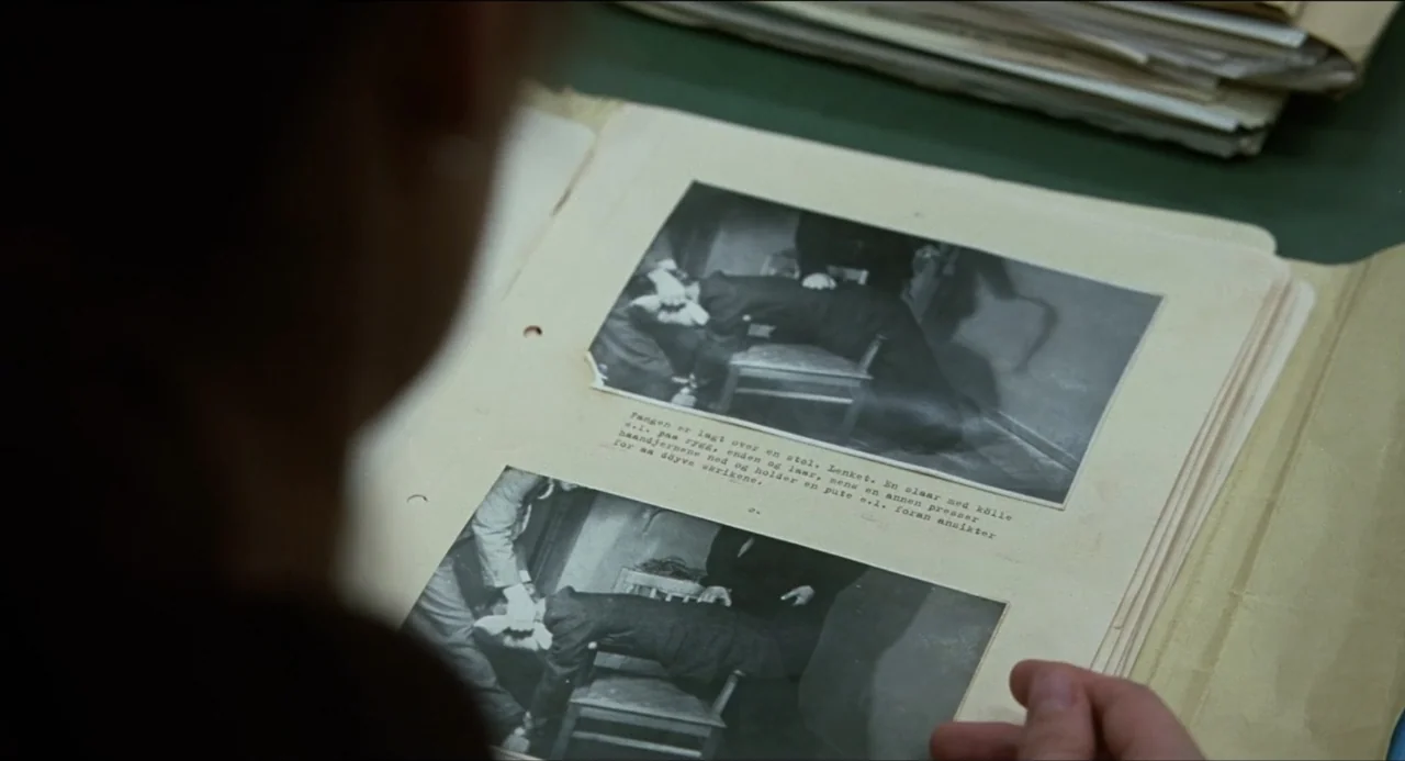 Sentimental Value (2025) movie still: medium — A person holds a binder containing archived black and white crime scene photographs. The photographs…
