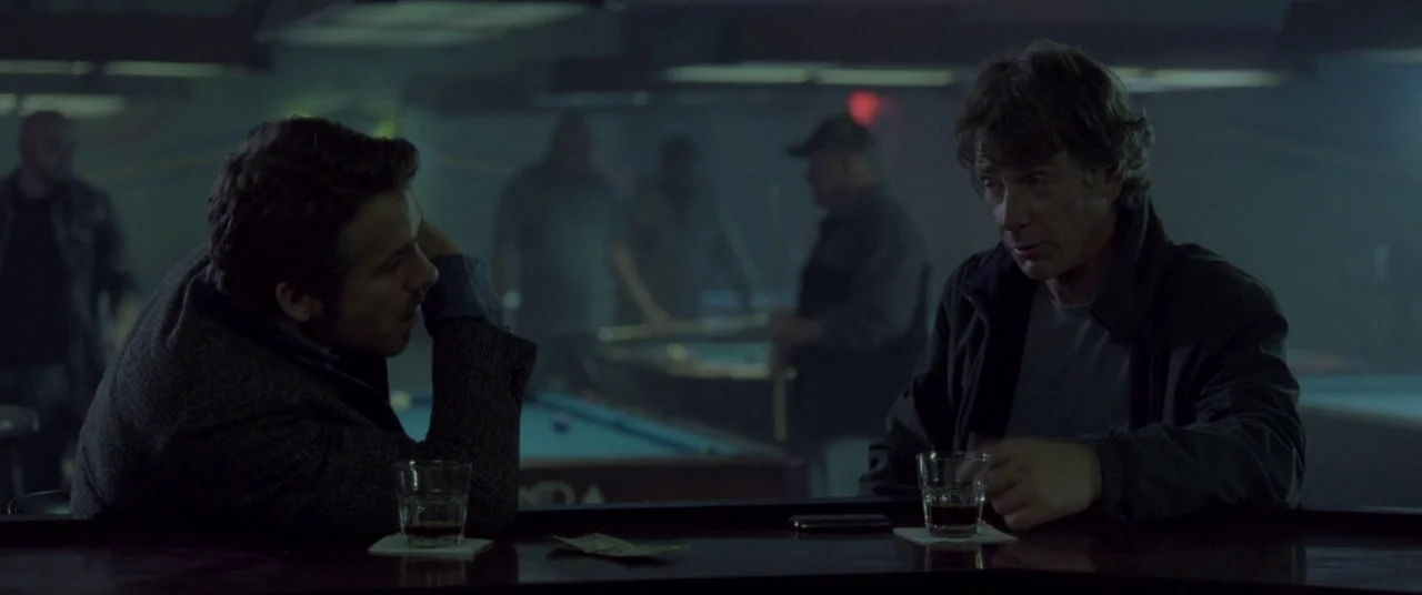 Mississippi Grind (2015) movie still: medium — A dimly lit pool hall with blurred figures in the background near tables. Two men sit at a bar…