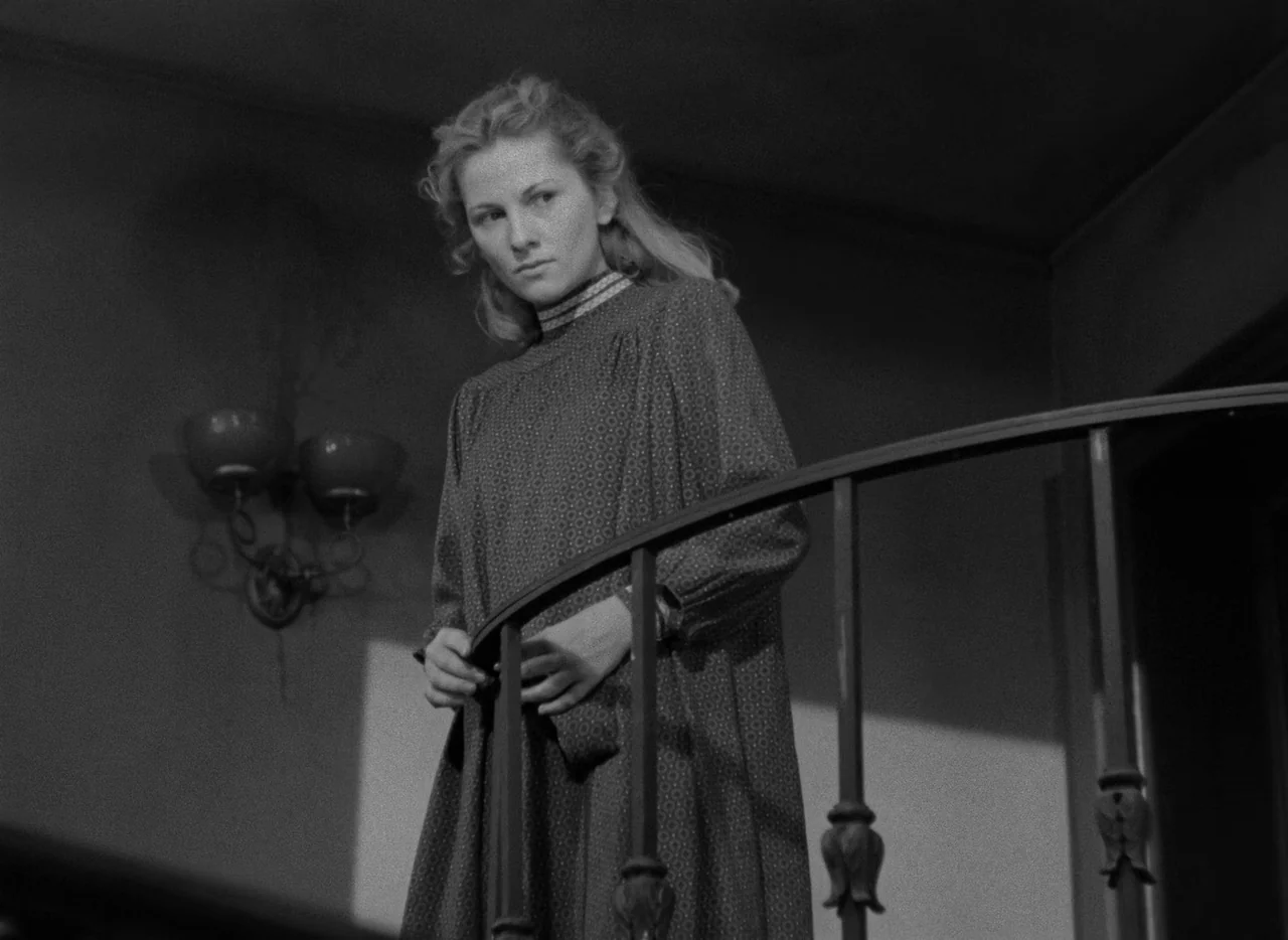 Letter From An Unknown Woman (1948) movie still: medium — A dimly lit upper level landing features a dark metal railing and a wall sconce. A young…