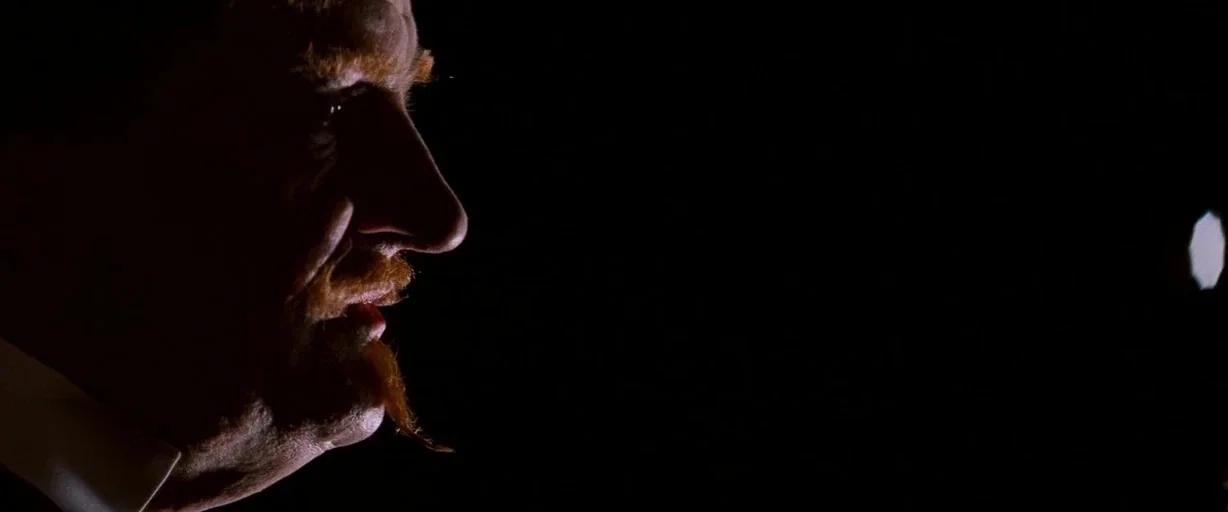 Moulin Rouge! (2001) movie still: closeup — An older man with a distinctive beard is shown in profile against darkness. Only the side of his face is…
