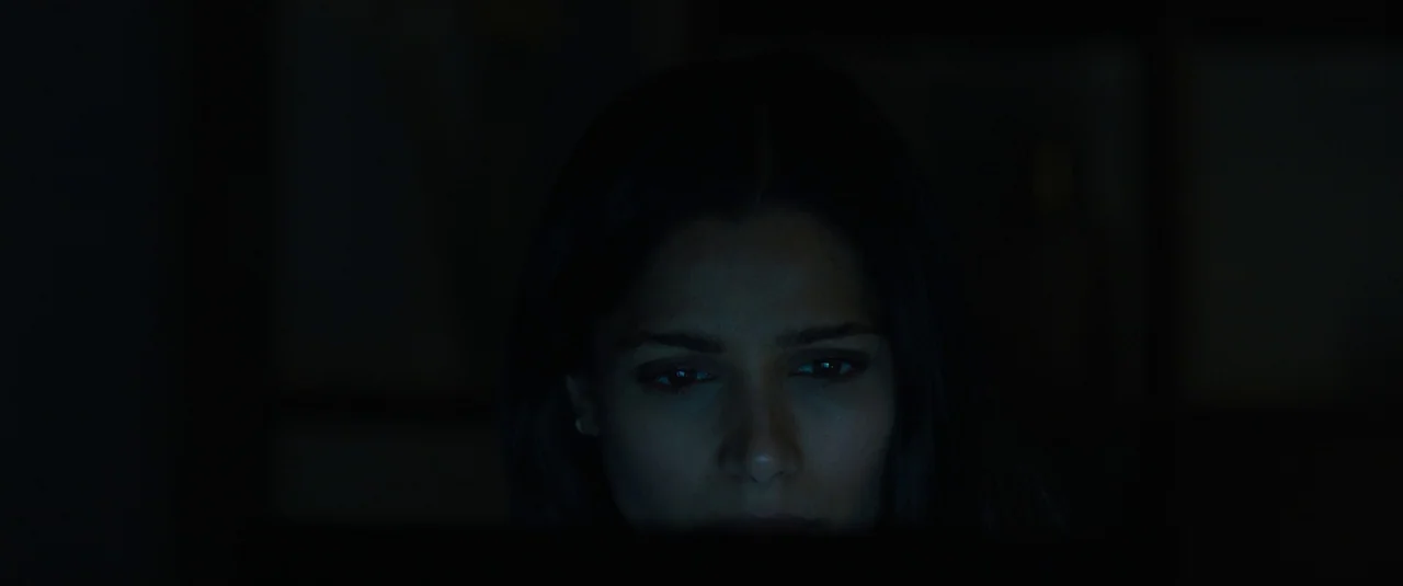 Intrusion (2021) movie still: closeup — A dark, dimly lit room is illuminated only by a source off-screen. A woman stares into the light, her face…