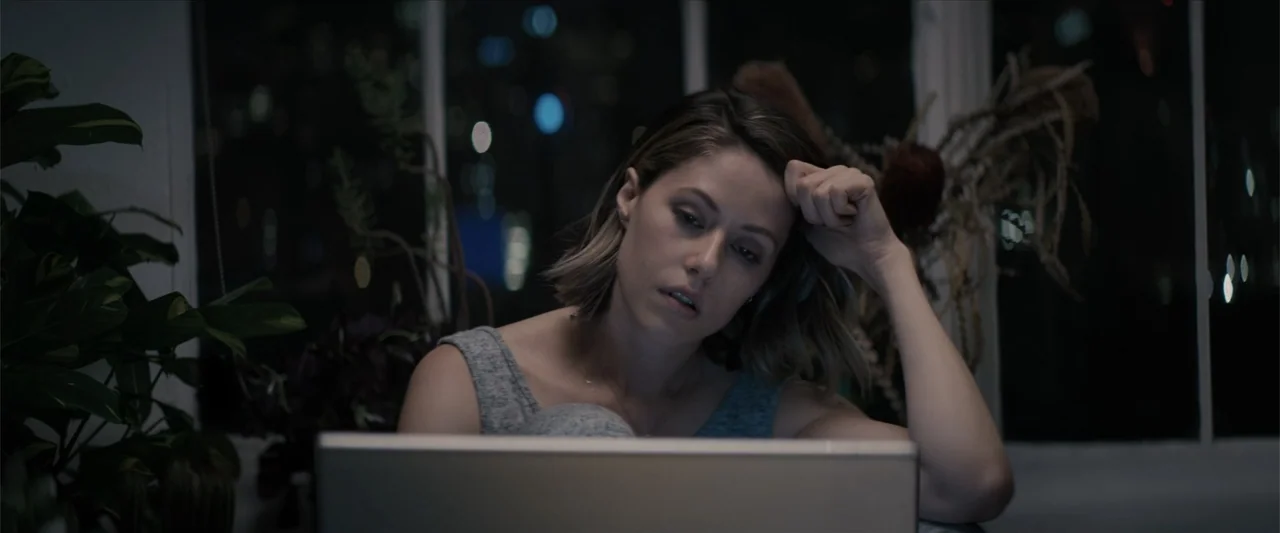 Equation of Love and Tone Deafness (2015) movie still: medium — A dimly lit room at night features a large window with out-of-focus city lights. A…