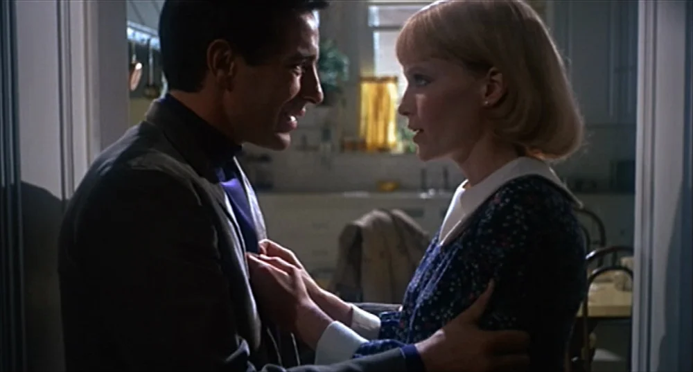 Rosemary’s Baby (1968) movie still: medium — A man and woman stand in a narrow transition space between two rooms. They are positioned face-to-face…